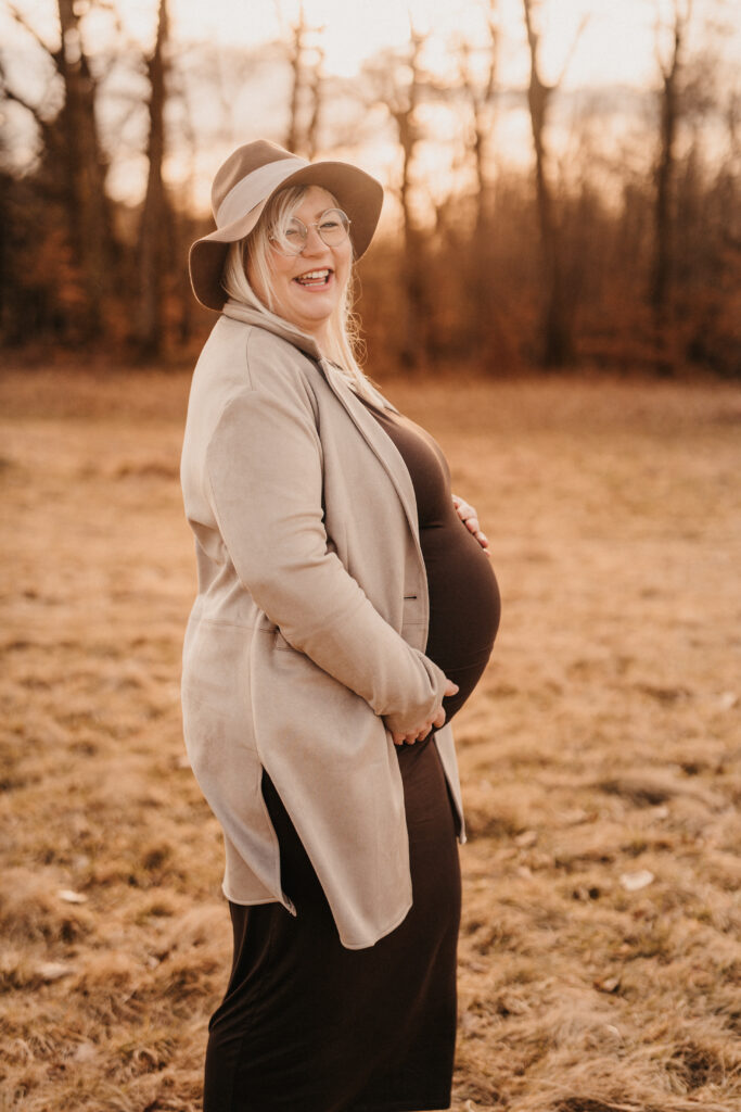 Schwangere Frau steht im Sonnenuntergang und hält ihren Babybauch fest